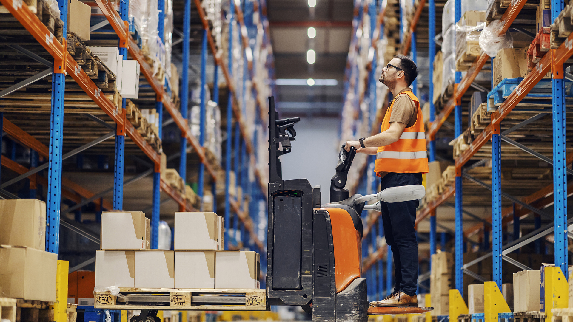 A forklift driver is collecting and organizing boxes with goods in storage.