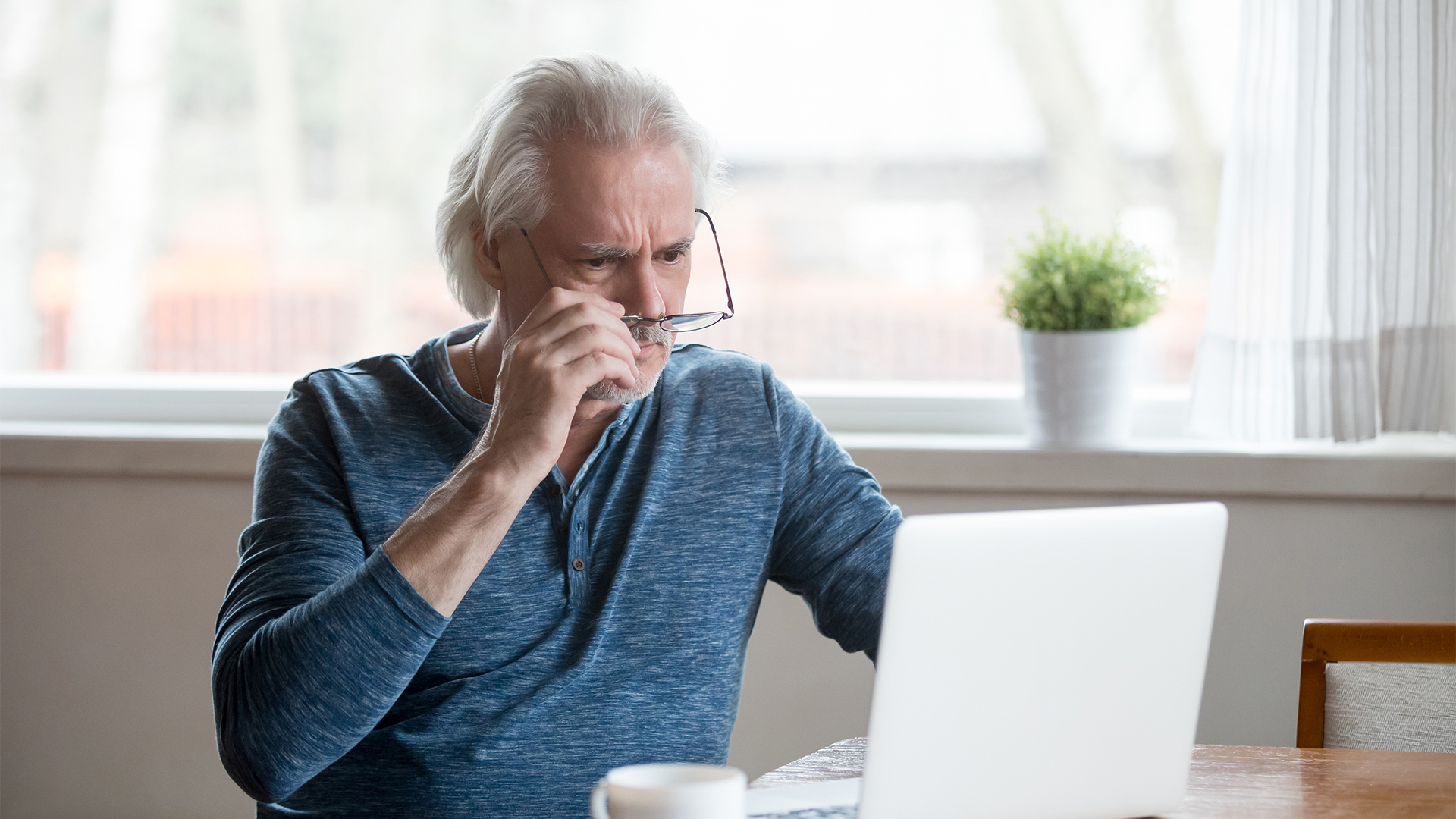 Shocked frustrated senior man taking off glasses looking at laptop