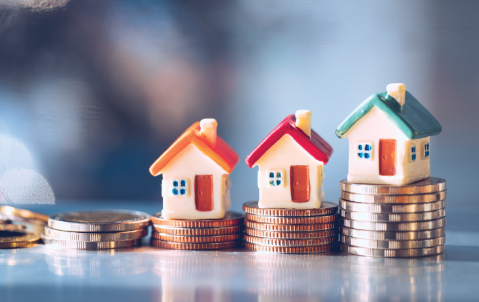 Miniature houses placed on stacks of coins represent real estate appreciation, investment growth, and capital gains tax planning.